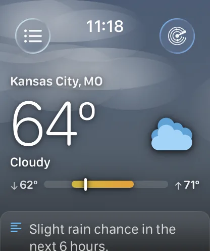 The Apple Watch main screen under an overcast grey-blue sky with soft haze bands, showing Kansas City, MO at 64 degrees and Cloudy, a range bar reading down-arrow 62 degrees on the left and up-arrow 71 degrees on the right