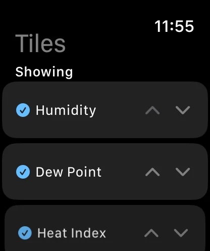 The Tiles screen on the watch, headed Tiles and Showing, with Humidity, Dew Point and Heat Index each ticked and carrying up and down chevrons.